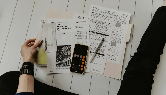 persona sosteniendo papel cerca de un bolígrafo y una calculadora